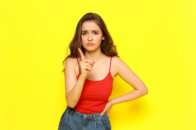 Una vista frontal joven y bella dama en camisa roja y jeans azul posando con expresión amenazadora