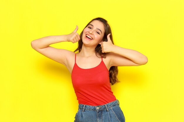 Una vista frontal joven bella dama en camisa roja y jeans azul posando con expresión de sonrisa