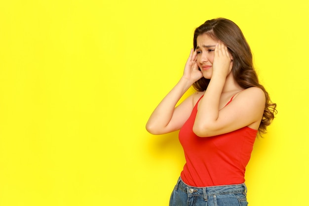 Una vista frontal joven bella dama en camisa roja y jeans azul posando con expresión triste