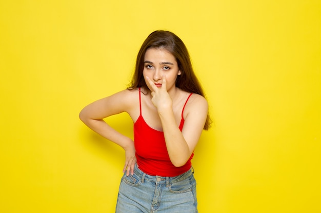 Una vista frontal joven y bella dama en camisa roja y jeans azul posando