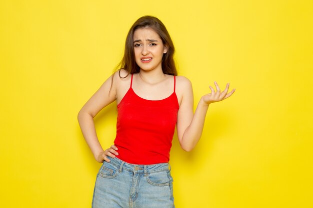 Una vista frontal joven y bella dama en camisa roja y jeans azul posando