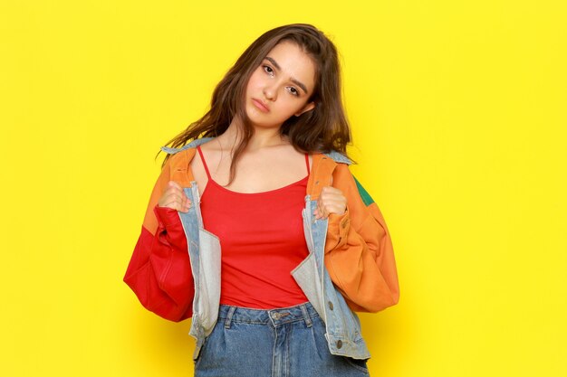 Una vista frontal joven y bella dama en chaqueta roja y jeans azul con expresión aburrida