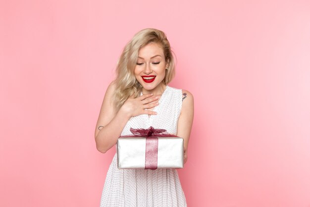 Una vista frontal joven bella dama en vestido blanco con caja actual con una sonrisa en su rostro