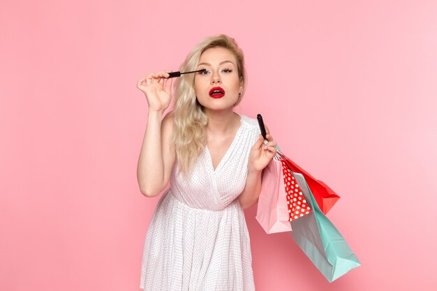 Una vista frontal joven y bella dama en vestido blanco con paquetes de compras y maquillaje