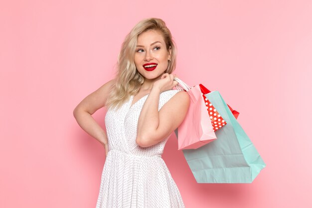 Una vista frontal joven y bella dama en vestido blanco con paquetes de compras con una sonrisa en su rostro