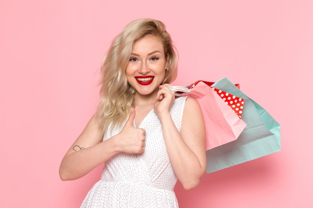 Una vista frontal joven y bella dama en vestido blanco con paquetes de compras con una sonrisa en su rostro