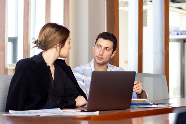 Una vista frontal joven y bella empresaria en camisa negra chaqueta negra junto con un joven discutiendo temas de trabajo dentro de su trabajo de trabajo de oficina
