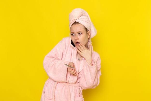 Una vista frontal joven y bella mujer en bata de baño rosa hablando por teléfono