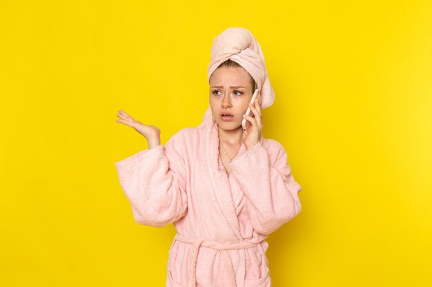 Una vista frontal joven y bella mujer en bata de baño rosa hablando por teléfono