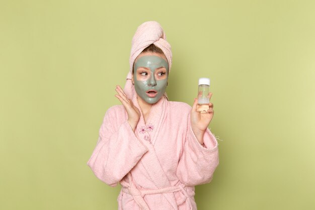 Una vista frontal joven y bella mujer en bata de baño rosa con mascarilla con frasco de spray