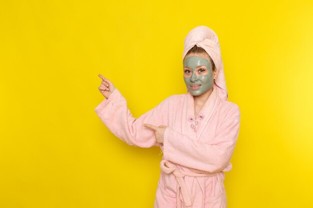 Una vista frontal joven y bella mujer en bata de baño rosa con mascarilla