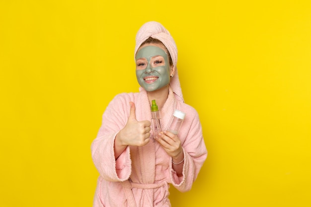 Una vista frontal joven y bella mujer en bata de baño rosa sosteniendo aerosoles sonriendo
