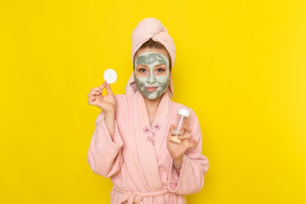 Una vista frontal joven y bella mujer en bata de baño rosa con spray limpiador de maquillaje