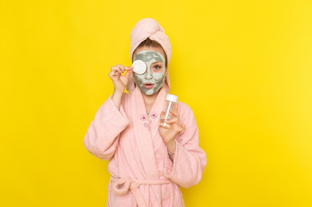 Una vista frontal joven y bella mujer en bata de baño rosa con spray limpiador de maquillaje