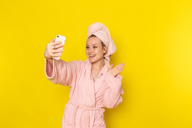 Una vista frontal joven y bella mujer en bata de baño rosa tomando un selfie con una sonrisa