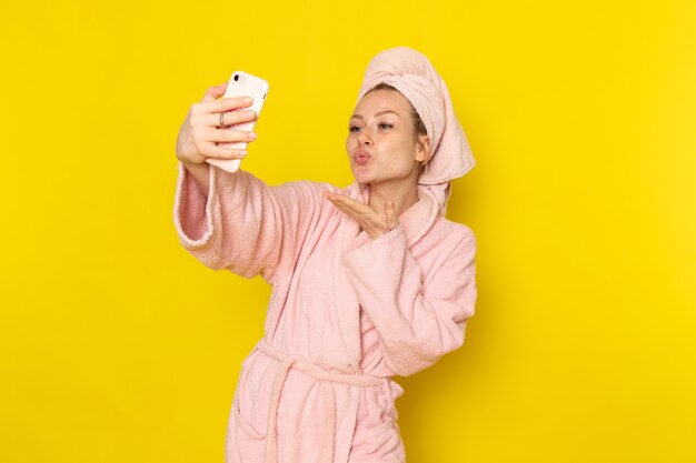 Una vista frontal joven y bella mujer en bata de baño rosa tomando un selfie