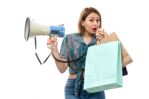 Una vista frontal joven y bella mujer en blusa de color azul jeans sosteniendo paquetes de compras con megáfono