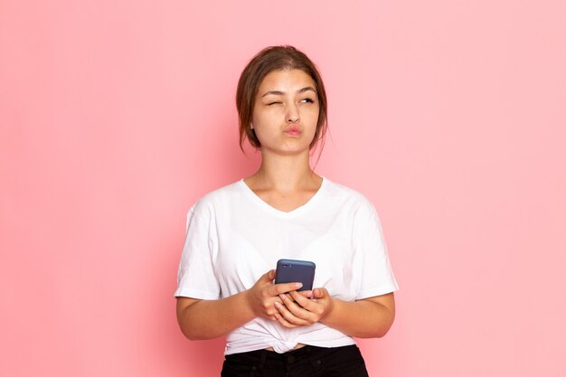 Una vista frontal joven y bella mujer en camisa blanca posando con expresión divertida y sosteniendo un teléfono