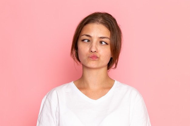 Una vista frontal joven y bella mujer en camisa blanca posando con expresión divertida