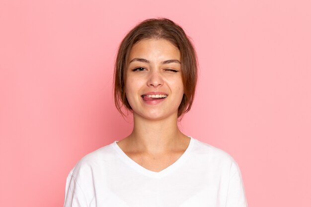 Una vista frontal joven y bella mujer en camisa blanca posando con expresión encantada y sonriente