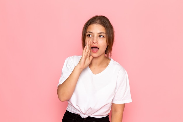 Una vista frontal joven y bella mujer en camisa blanca posando susurrando y llamando