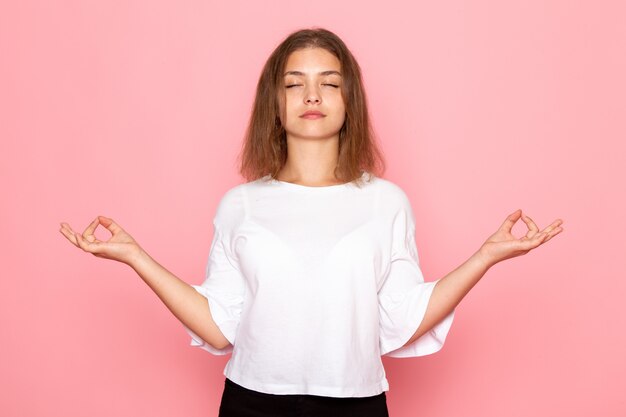 Una vista frontal joven y bella mujer en camisa blanca en pose de meditación