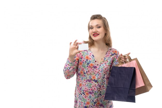 Una vista frontal joven y bella mujer en camisa de flores y pantalón negro con paquetes de compras mostrando tarjeta blanca