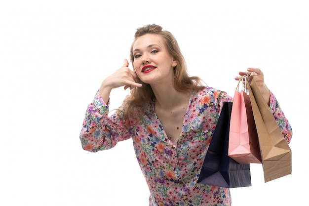 Una vista frontal joven y bella mujer en camisa de flores y pantalones negros con paquetes de compras mostrando gesto de llamada telefónica