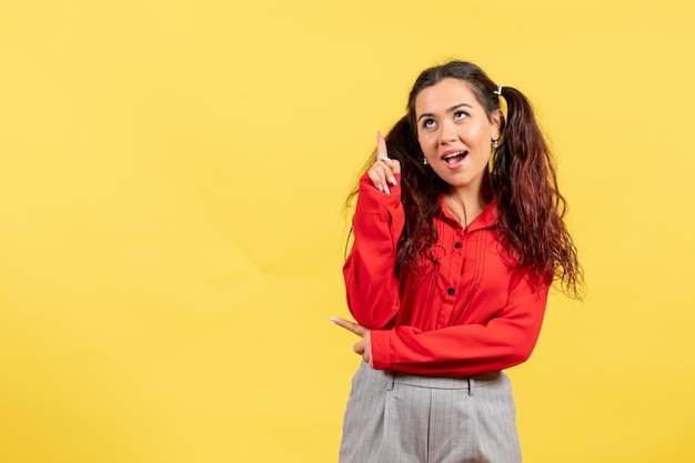 Vista frontal joven en blusa roja con cabello lindo apuntando sobre fondo amarillo inocencia infantil color niño niña juventud