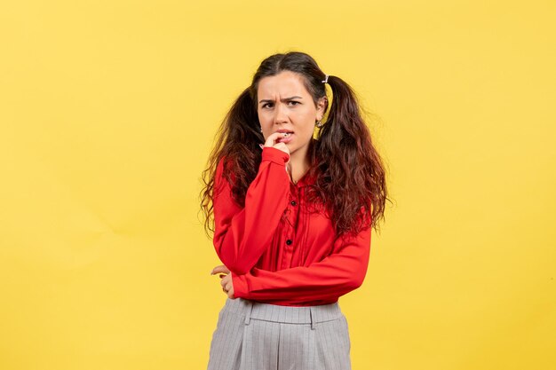 Vista frontal joven en blusa roja con cabello lindo y cara nerviosa sobre fondo amarillo niño niña juventud inocencia color