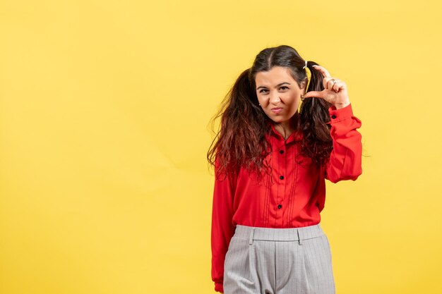 Vista frontal joven en blusa roja con cabello lindo que muestra el tamaño sobre fondo amarillo inocencia niño niña color juvenil