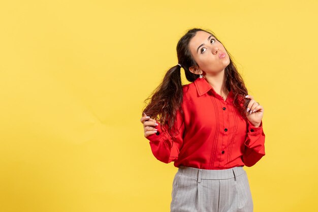 Vista frontal joven en blusa roja con lindo cabello y cara de coqueta sobre fondo amarillo inocencia niño niña color juvenil