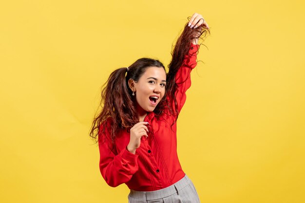 Vista frontal joven en blusa roja con pelo lindo posando sobre fondo amarillo niño niña juventud inocencia color niño