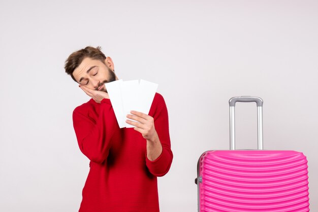 Vista frontal joven con bolsa rosa y sosteniendo boletos sintiéndose cansado en la pared blanca viaje vuelo color viaje turista vacaciones foto emoción