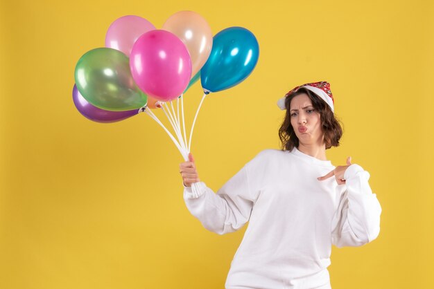 Vista frontal joven bonita mujer sosteniendo globos en amarillo navidad año nuevo color mujer emoción