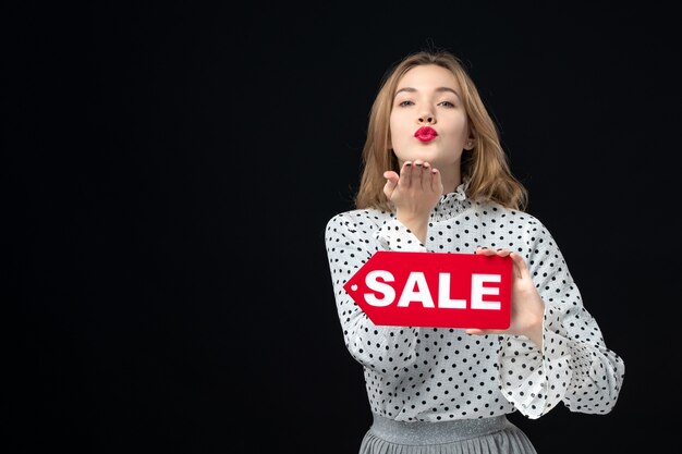 Foto gratuita vista frontal joven bonita mujer sosteniendo venta escribiendo en la pared negra color compras mujer emoción rojo moda