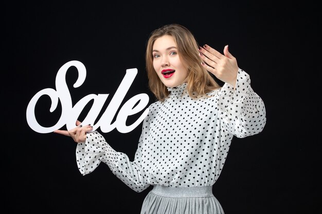 Vista frontal joven bonita mujer sosteniendo venta escribiendo en una pared negra compras belleza emoción modelo de color foto moda
