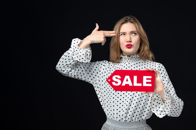 Vista frontal joven bonita mujer sosteniendo venta escribiendo en la pared negra emoción rojo compras foto moda mujer color