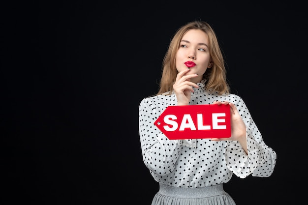 Foto gratuita vista frontal joven bonita mujer sosteniendo venta escribiendo en la pared negra emoción rojo compras foto moda mujer colores