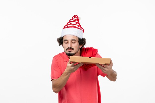 Vista frontal del joven con caja de comida de entrega en la pared blanca