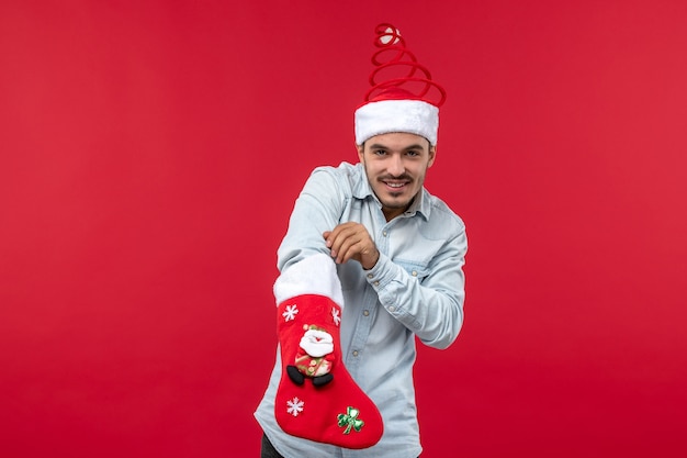 Vista frontal del joven con calcetín de Navidad en la pared roja