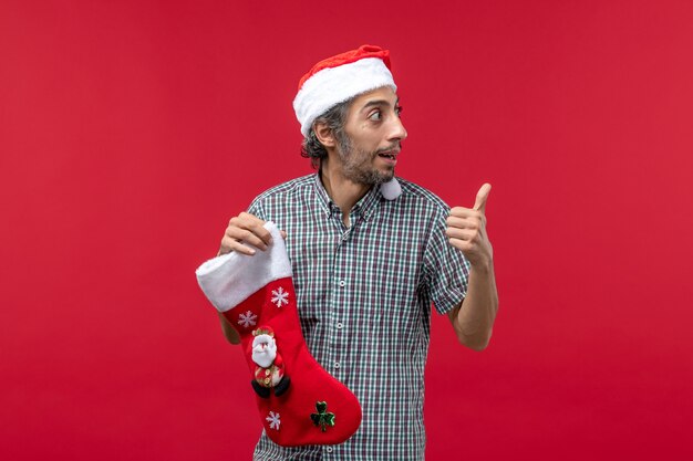 Foto gratuita vista frontal del joven con calcetín de navidad en la pared roja