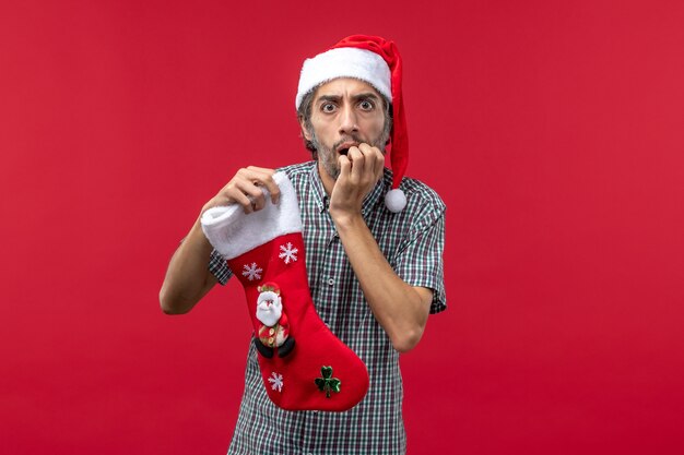 Vista frontal del joven con calcetín de Navidad en la pared roja