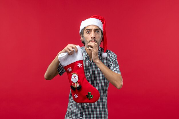 Vista frontal del joven con calcetín de Navidad en la pared roja