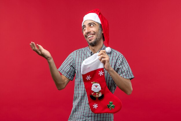 Vista frontal del joven con calcetín de Navidad en la pared roja
