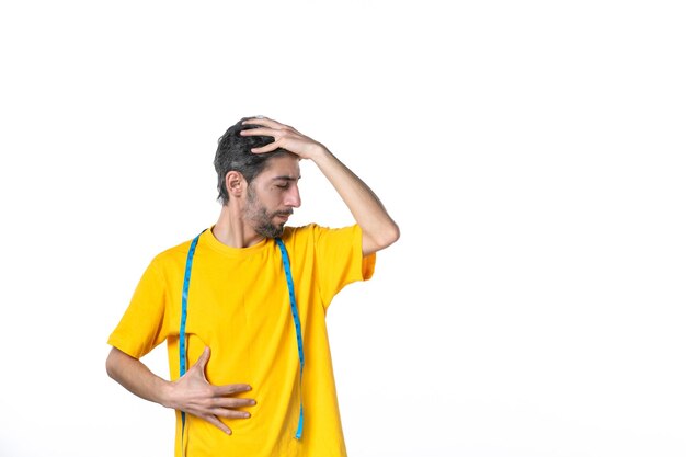 Vista frontal del joven con camisa amarilla y sosteniendo el medidor sintiéndose cansado en la superficie blanca