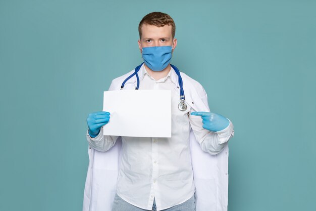Una vista frontal joven en camisa blanca y guantes azules con máscara azul con papel en el espacio azul