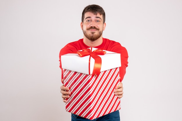 Foto gratuita vista frontal del joven en camisa roja con regalo de navidad en caja en pared blanca