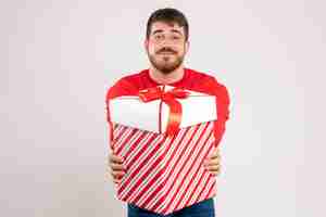 Foto gratuita vista frontal del joven en camisa roja con regalo de navidad en caja en pared blanca