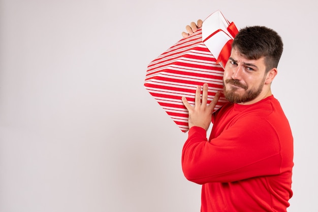 Foto gratuita vista frontal del joven en camisa roja con regalo de navidad en caja en pared blanca